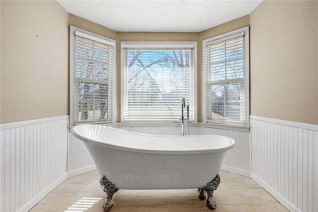 bathroom with a wainscoted wall, a textured ceiling, and a freestanding tub