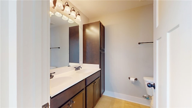 bathroom with toilet, double vanity, baseboards, and a sink