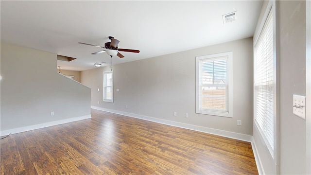 empty room with ceiling fan, visible vents, dark wood finished floors, and baseboards