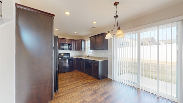 kitchen with light stone counters, dark wood-style floors, decorative light fixtures, a healthy amount of sunlight, and black appliances