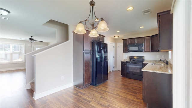 kitchen featuring light stone counters, dark wood-style flooring, black appliances, pendant lighting, and a sink