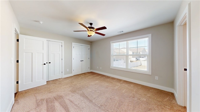 unfurnished bedroom featuring light carpet, visible vents, baseboards, and multiple closets