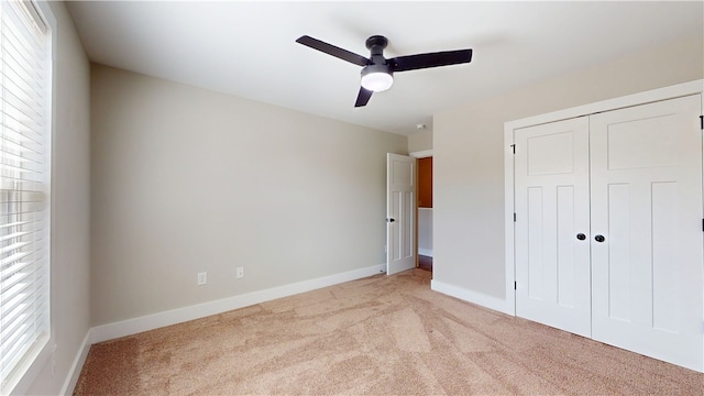 unfurnished bedroom featuring light carpet, ceiling fan, baseboards, and a closet