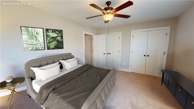 bedroom featuring light carpet, a ceiling fan, and multiple closets