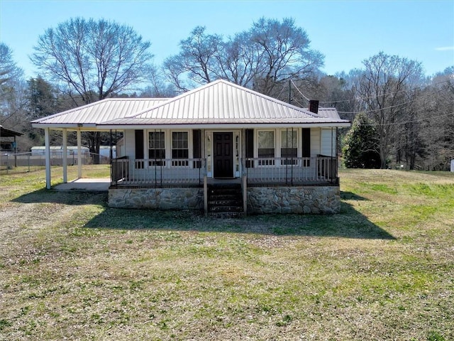 farmhouse with covered porch, metal roof, a front lawn, and a chimney