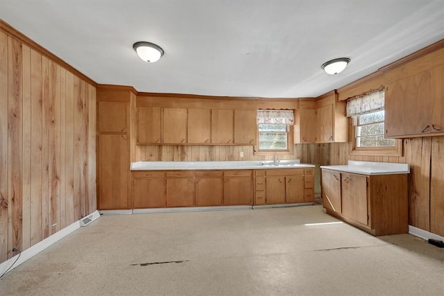 kitchen featuring light countertops, brown cabinetry, wood walls, a sink, and baseboards