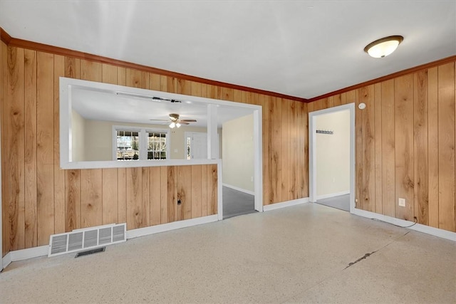 unfurnished living room with ornamental molding, visible vents, wood walls, and baseboards