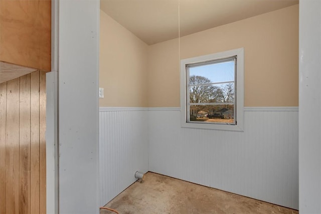 empty room with a wainscoted wall and unfinished concrete flooring