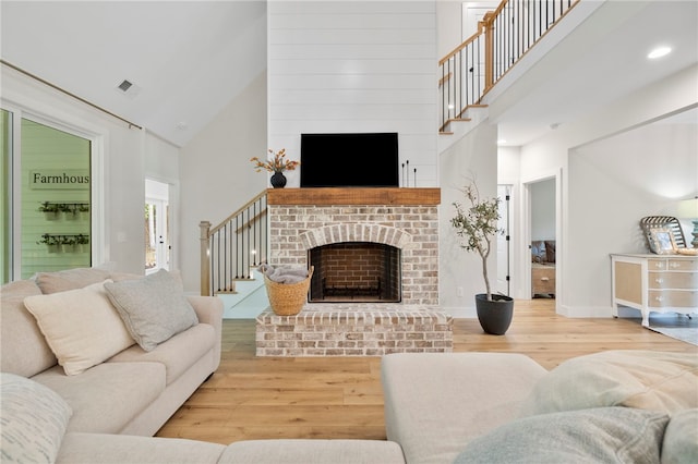 living room featuring stairs, light wood finished floors, a fireplace, and a towering ceiling