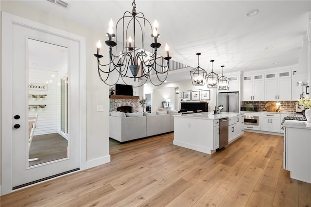 kitchen featuring a center island with sink, light countertops, glass insert cabinets, open floor plan, and white cabinetry