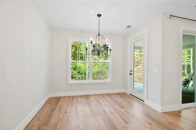 unfurnished dining area with baseboards, an inviting chandelier, visible vents, and light wood-style floors