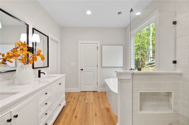 full bathroom with a freestanding tub, recessed lighting, wood finished floors, a sink, and double vanity