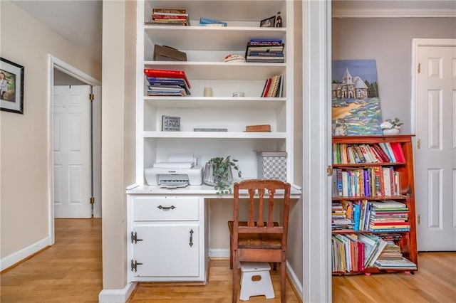 home office featuring baseboards, light wood-style flooring, and built in desk