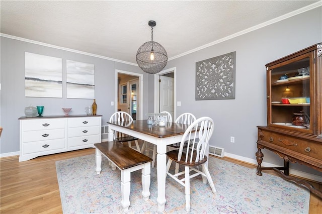 dining space featuring light wood-style flooring, baseboards, a textured ceiling, and ornamental molding