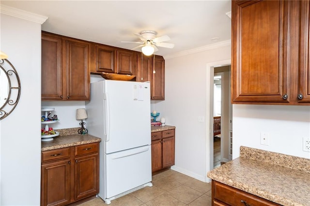 kitchen featuring light tile patterned floors, brown cabinetry, a ceiling fan, freestanding refrigerator, and crown molding