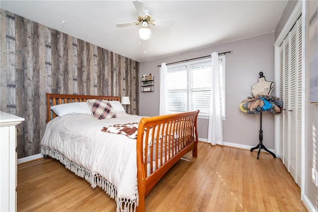 bedroom featuring baseboards, light wood-style flooring, ceiling fan, a closet, and wood walls