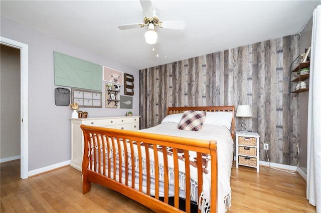 bedroom featuring a ceiling fan, an accent wall, baseboards, and wood finished floors