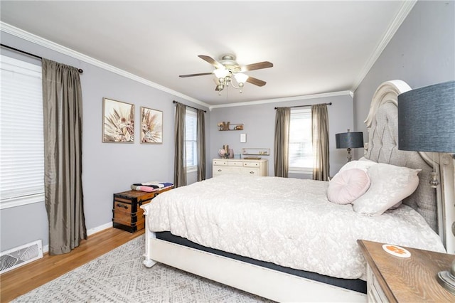 bedroom with a ceiling fan, baseboards, wood finished floors, visible vents, and ornamental molding