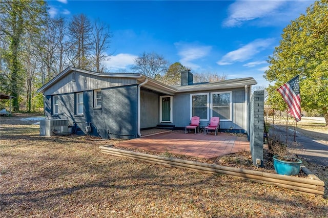 back of house featuring a patio area, central AC unit, a chimney, and brick siding