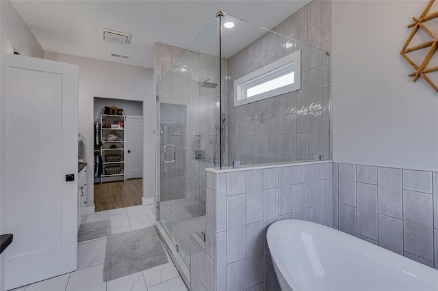 bathroom with marble finish floor, tile walls, a soaking tub, a spacious closet, and a stall shower