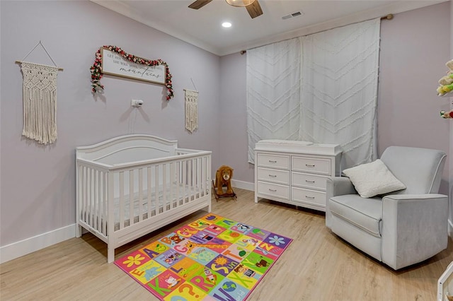 bedroom featuring a nursery area, baseboards, visible vents, and light wood-style floors