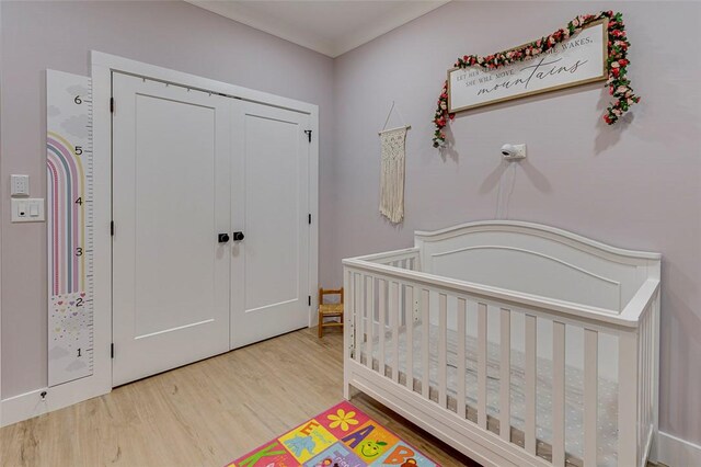 bedroom with a nursery area, a closet, and wood finished floors