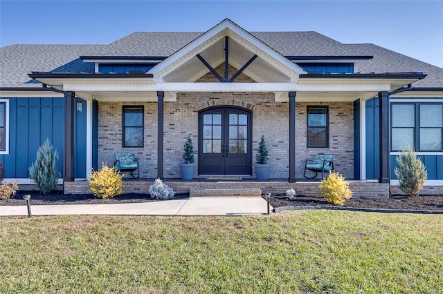 view of front of house featuring a front lawn, covered porch, brick siding, and french doors