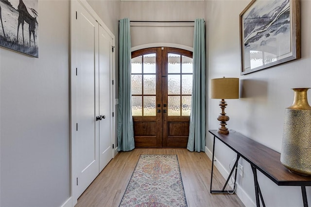 entrance foyer featuring arched walkways, french doors, light wood-style flooring, and baseboards