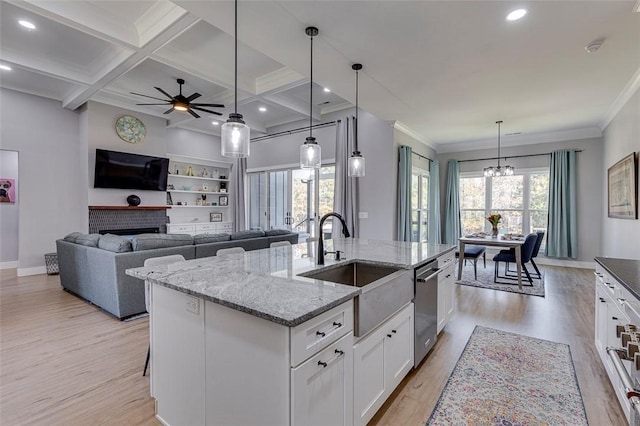 kitchen featuring light wood-style flooring, a sink, a kitchen island with sink, a fireplace, and stainless steel dishwasher