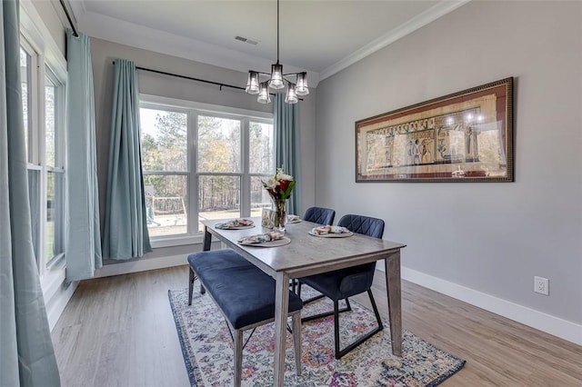 dining area with baseboards, visible vents, ornamental molding, light wood-type flooring, and a chandelier