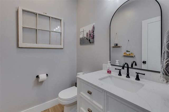 half bath featuring baseboards, vanity, toilet, and wood finished floors