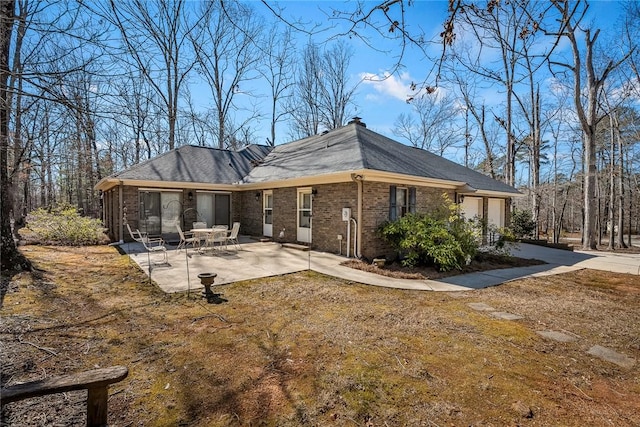 rear view of house with brick siding, a lawn, an attached garage, a patio area, and driveway