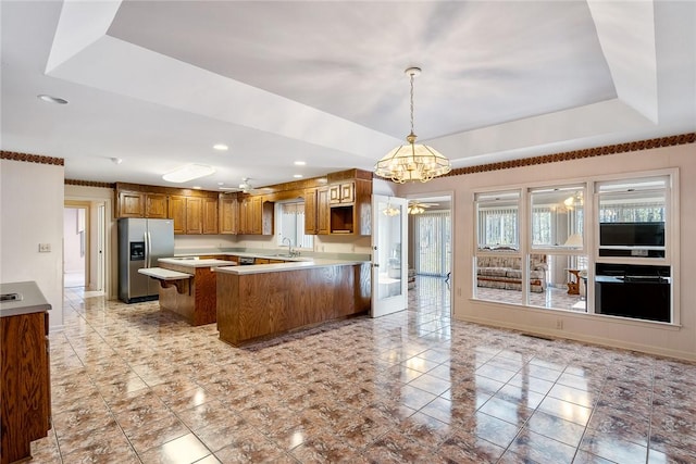 kitchen featuring a peninsula, a tray ceiling, stainless steel fridge, and light countertops