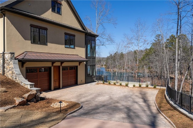 view of home's exterior featuring metal roof, an attached garage, a standing seam roof, fence, and decorative driveway