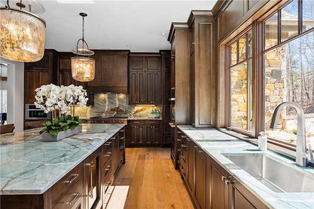 kitchen with light stone countertops, dark brown cabinetry, a sink, and decorative light fixtures