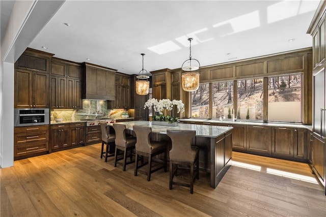 kitchen with pendant lighting, stainless steel appliances, a kitchen island, light stone countertops, and light wood-type flooring