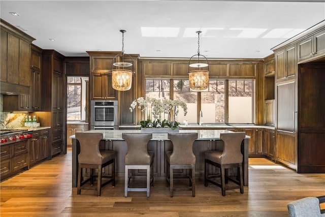 kitchen with a center island, decorative light fixtures, a sink, dark brown cabinets, and light stone countertops