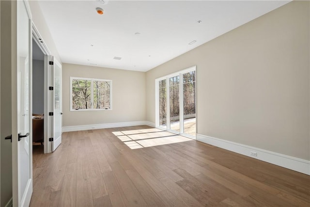 spare room featuring plenty of natural light, light wood-style flooring, and baseboards