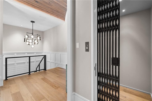 hall featuring light wood finished floors, a wainscoted wall, an upstairs landing, a chandelier, and a decorative wall