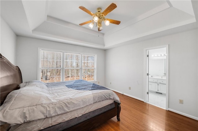 bedroom with baseboards, a tray ceiling, wood finished floors, and ensuite bathroom