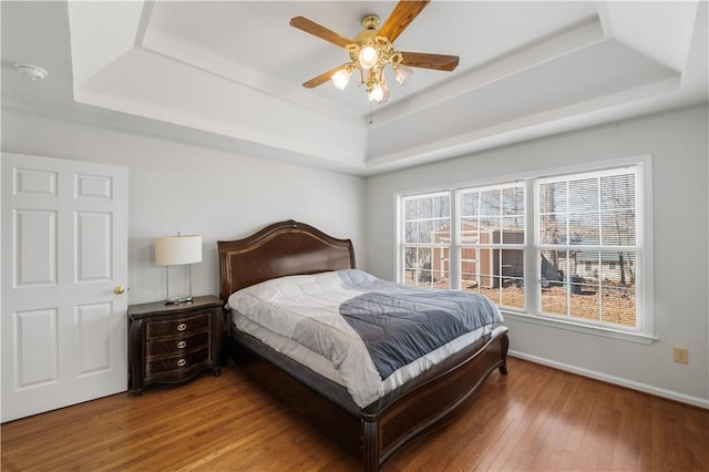 bedroom featuring wood-type flooring, a tray ceiling, ceiling fan, and baseboards