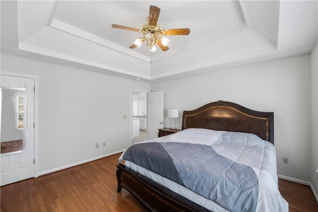 bedroom featuring ceiling fan, a tray ceiling, dark wood-style flooring, and baseboards