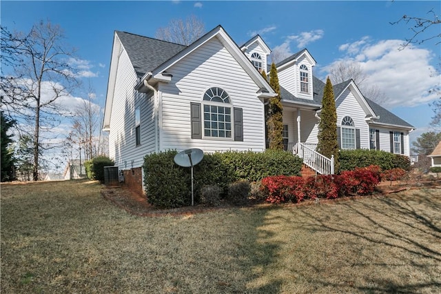 view of front facade with a shingled roof, a front yard, and central air condition unit