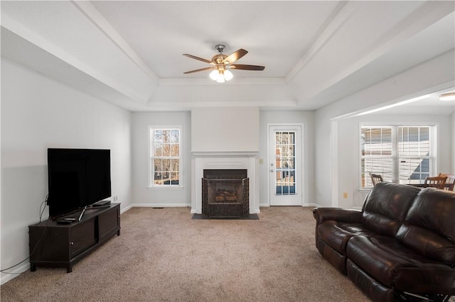 living area with a fireplace with flush hearth, a raised ceiling, a healthy amount of sunlight, and light carpet