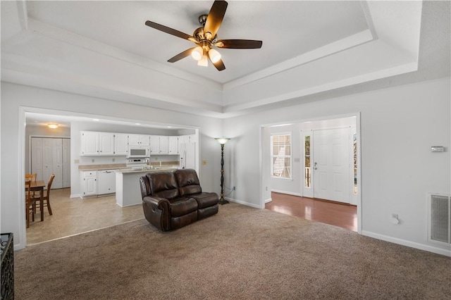 living area featuring light carpet, visible vents, baseboards, a ceiling fan, and a tray ceiling