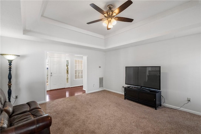 carpeted living area with baseboards, visible vents, a raised ceiling, and a ceiling fan