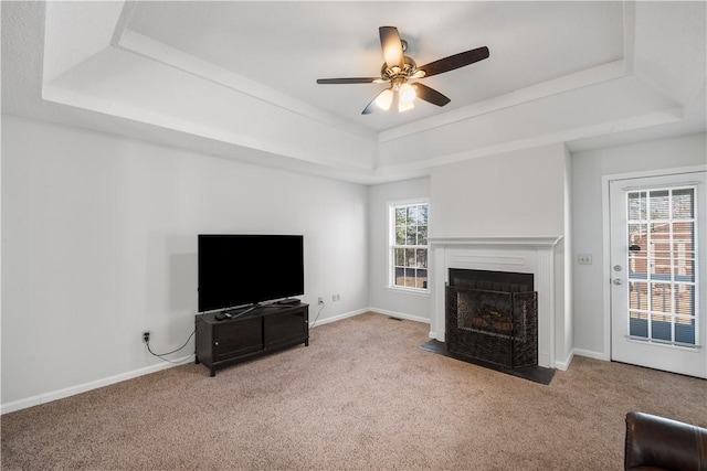 carpeted living area featuring a fireplace with flush hearth, a raised ceiling, a ceiling fan, and baseboards