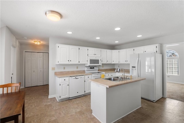 kitchen featuring light countertops, white cabinetry, a sink, an island with sink, and white appliances