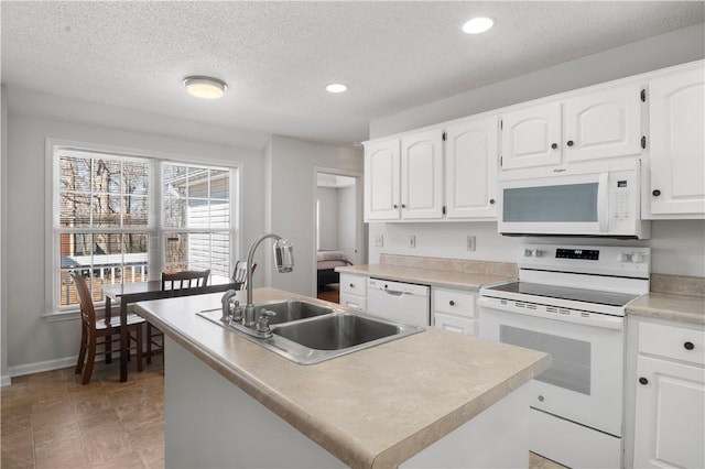 kitchen with white appliances, a center island with sink, white cabinets, light countertops, and a sink