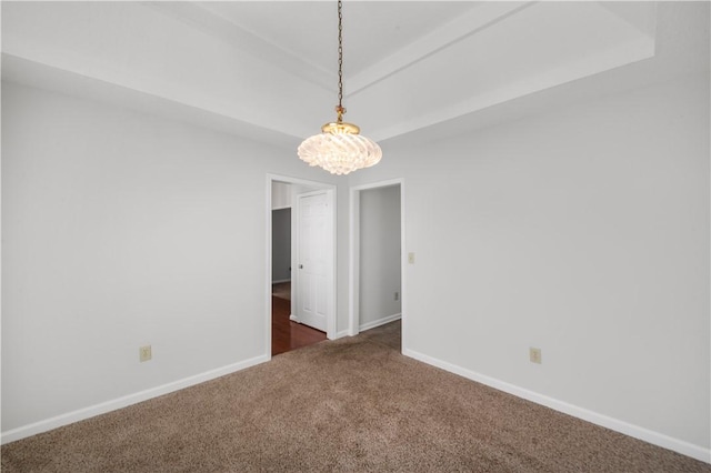 empty room featuring a notable chandelier, dark carpet, a raised ceiling, and baseboards